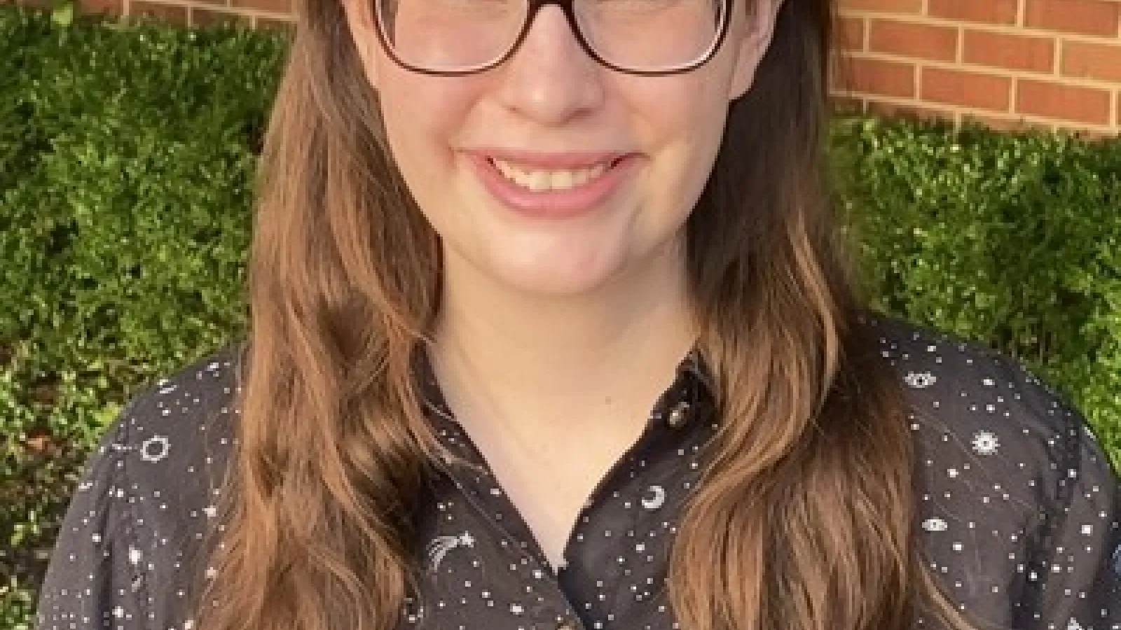 head and shoulders shot of Madison VonDeylen in front of brick wall and tree