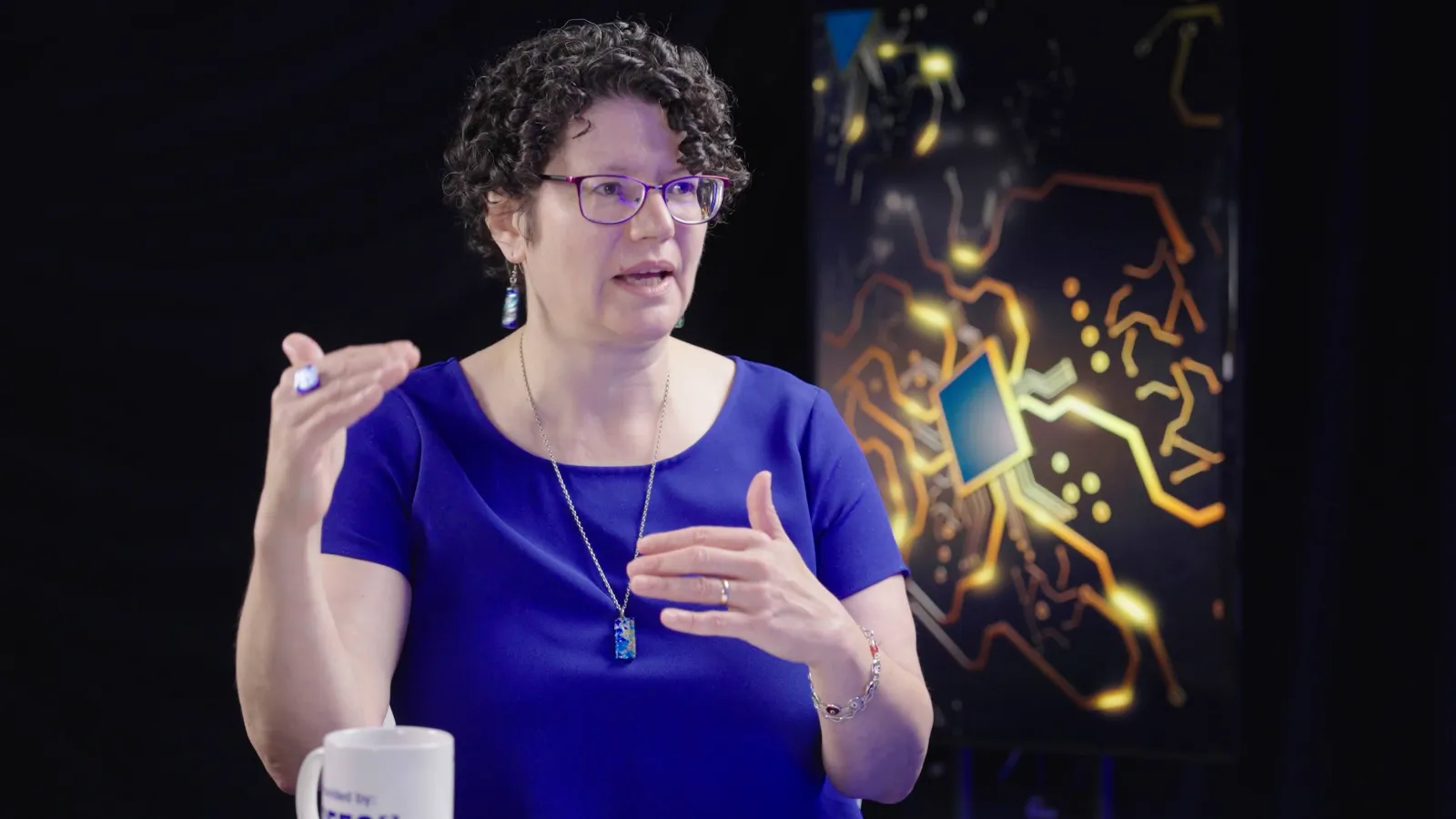 head and shoulder photo of Berger-Wolfe speaking in front of black background with image of computer chip graphic