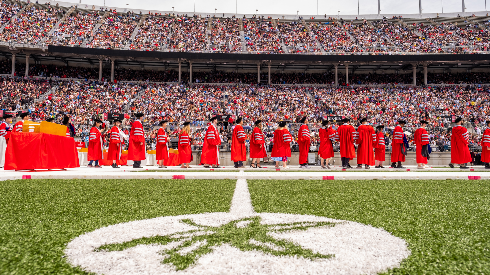 worms eye view of graduates in red gowns crossing field at stadium
