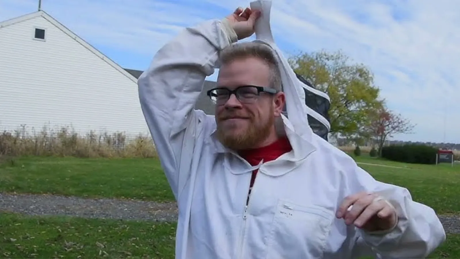 David Hibler outdoors wearing bee suit and removing head covering
