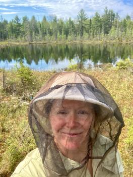 headshot of Jessie Lanterman Novotny standing in field and wearing hat with mosquito netting