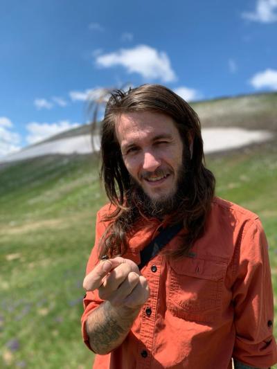 Cody standing outside in North Macedonia during his PhD holding Calosoma (Callisthenes) relictum specimen