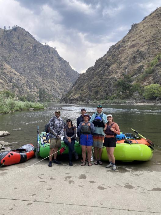 A group of slightly disheveled scientists stand in front of rafts and gear.