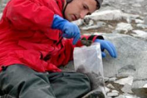 Nick Teets sitting on rocks collecting samples in the Antarctic